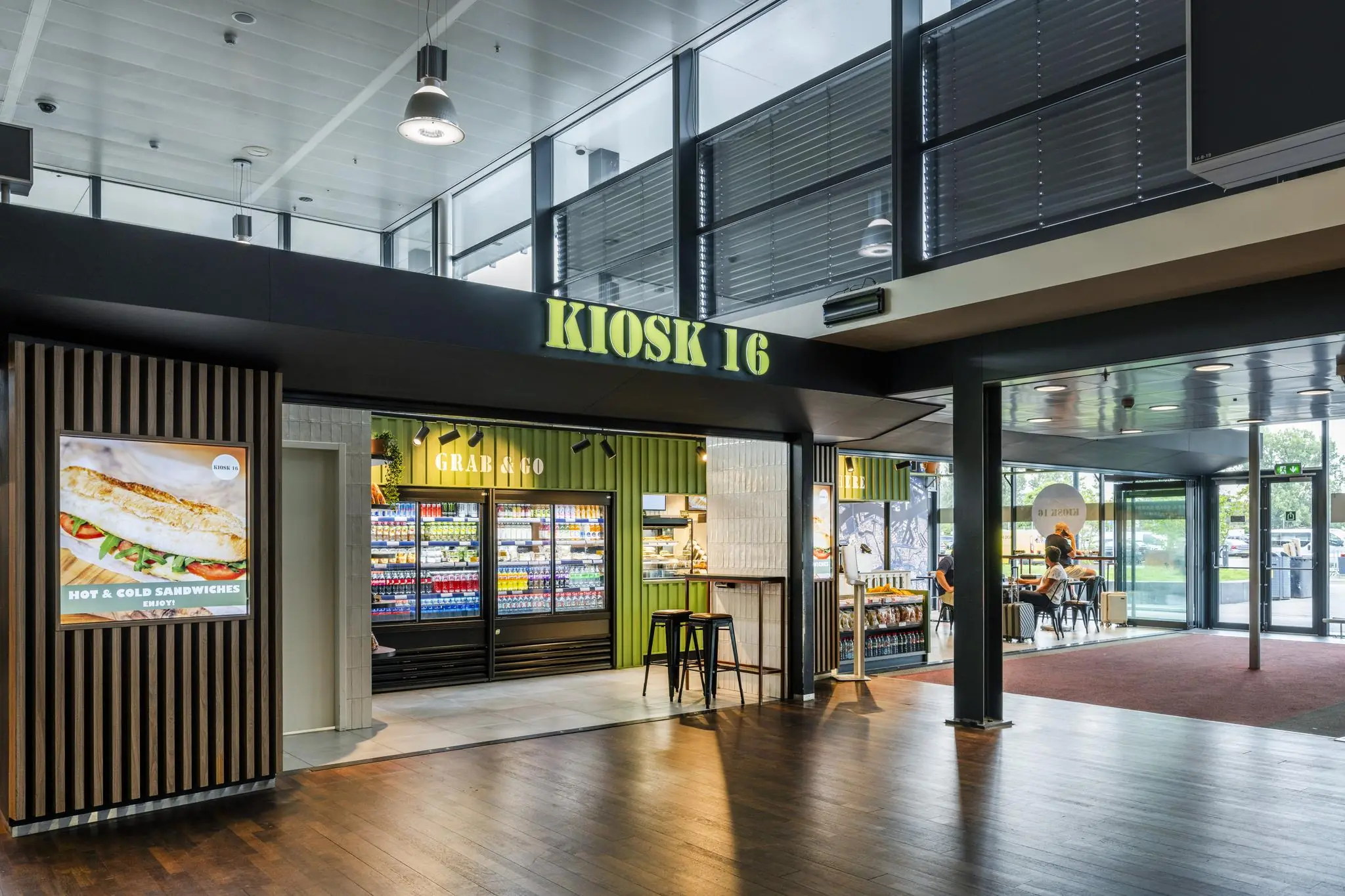 Moderne kiosk met de naam "Kiosk 16" op Rotterdam The Hague Airport, met een Grab & Go-verkooppunt en zitgedeelte.